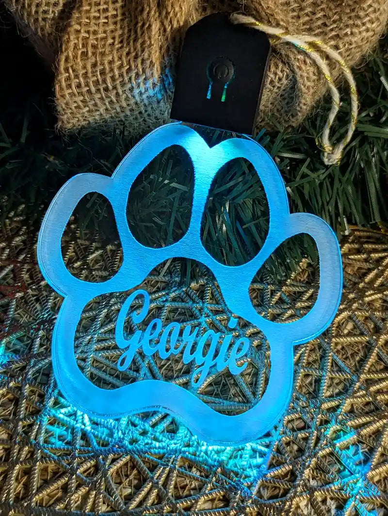 Blue paw-shaped ornament with name engraved, on a textured surface.
