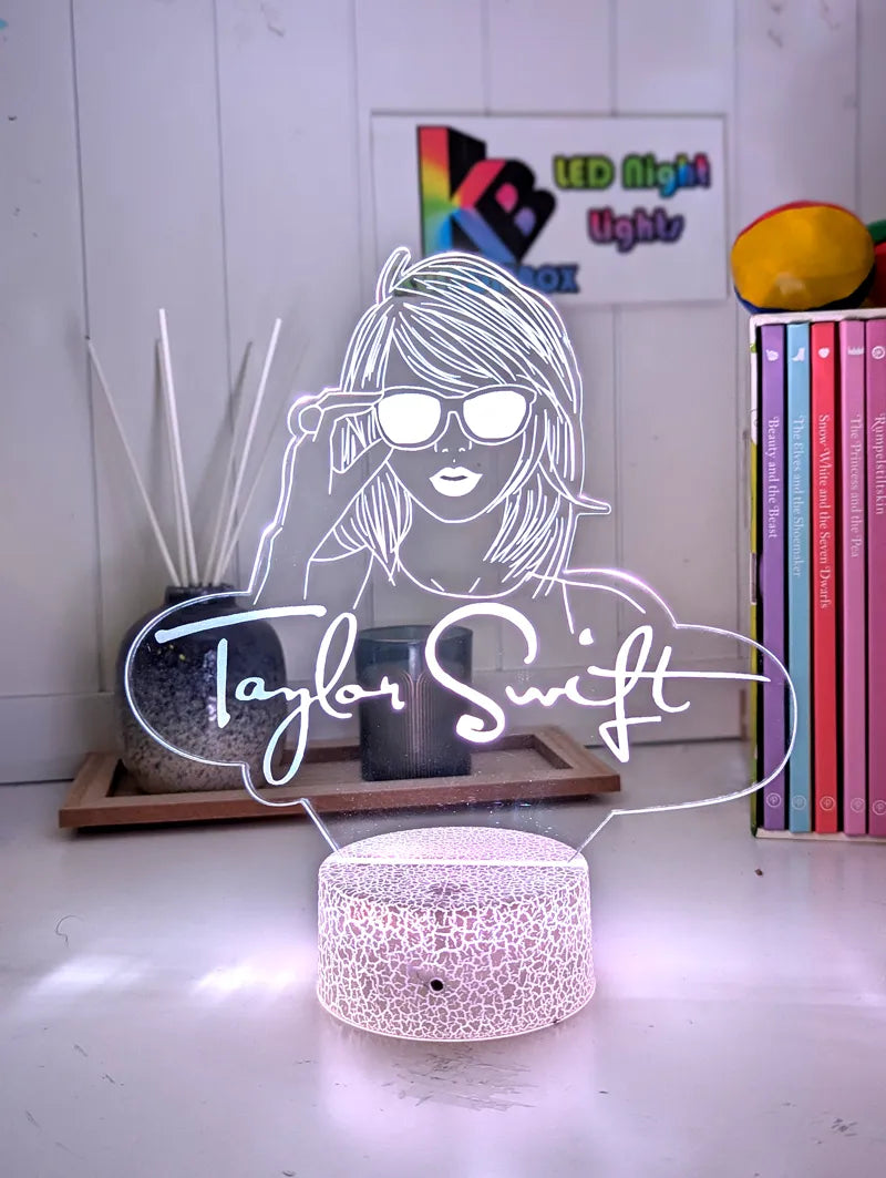 LED night light with a design of a person wearing sunglasses and the name 'Taylor Swift' below it, on a white surface.
